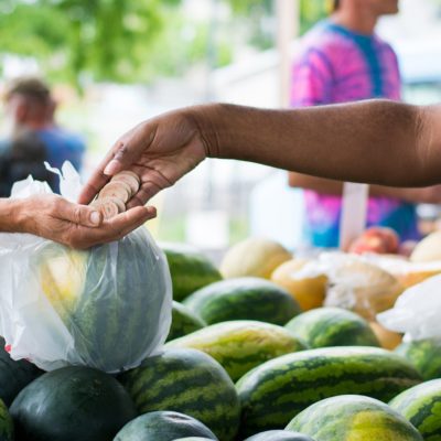 Two hands exchanging farmers market tokens over some watermelons